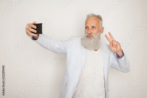 Old bearded active man taking selfie with mobile phone on white background