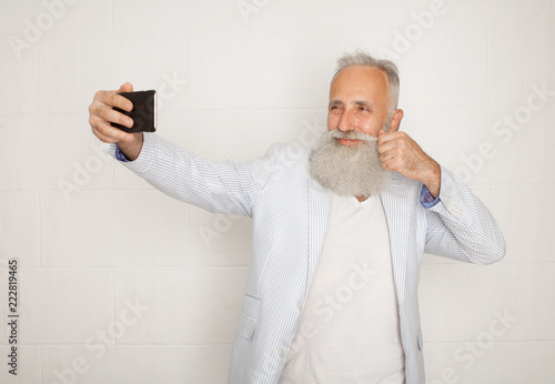 Old bearded active man taking selfie with mobile phone on white background