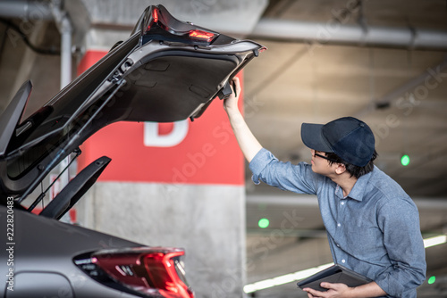 Young Asian auto mechanic holding digital tablet checking tailgate in auto service garage. Mechanical maintenance engineer working in automotive industry. Automobile servicing and repair concept