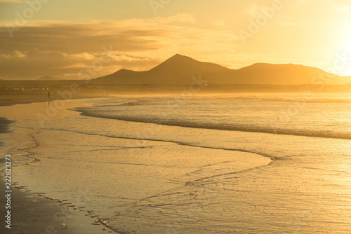 Golden sunset in pastel colors over the ocean strip of low tide with volcanoes on the horizon