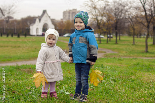 Осень,брат и сестра держатся за руки с жёлтыми листьями в парке