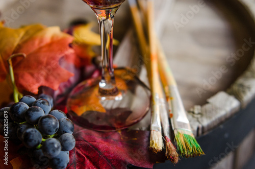 Glass of red wine, grapes and paint brushes on a wine barrel