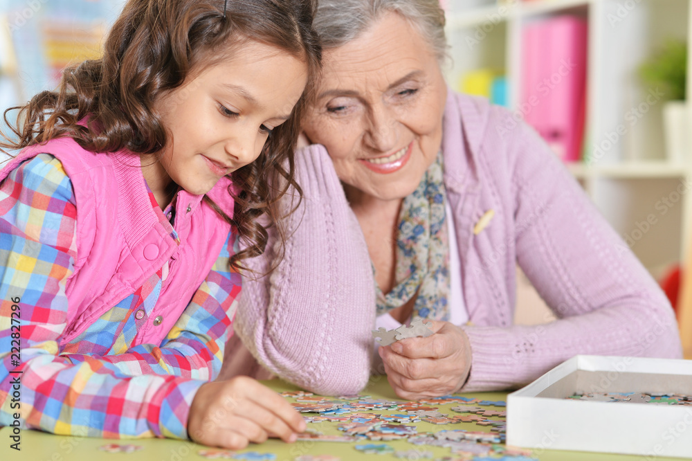 grandmother with little daughter collecting puzzle at home