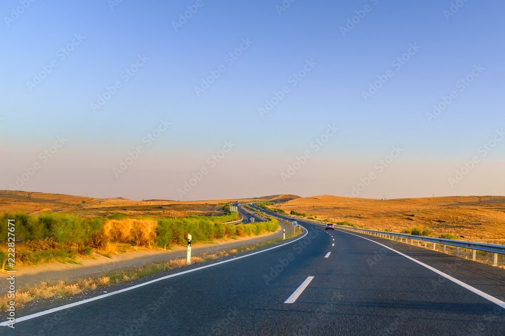 Driving along empty roads in Andalucia, Spain near Extremadura at the end of the summer with a golden sunrise lighting the dry fields and a blue sky. A road trip adventure
