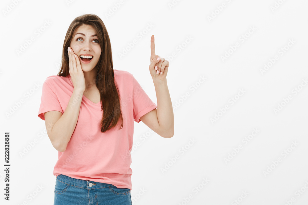 Look, I adore this copy space. Amazed good-looking optimistic woman in casual outfit, pointing and looking up while smiling broadly, holding palm near opened mouth and gasping from surprise Look, I adore this copy space. Amazed good-looking optimistic woman in casual outfit, pointing and looking up while smiling broadly, holding palm near opened mouth and gasping from surprise