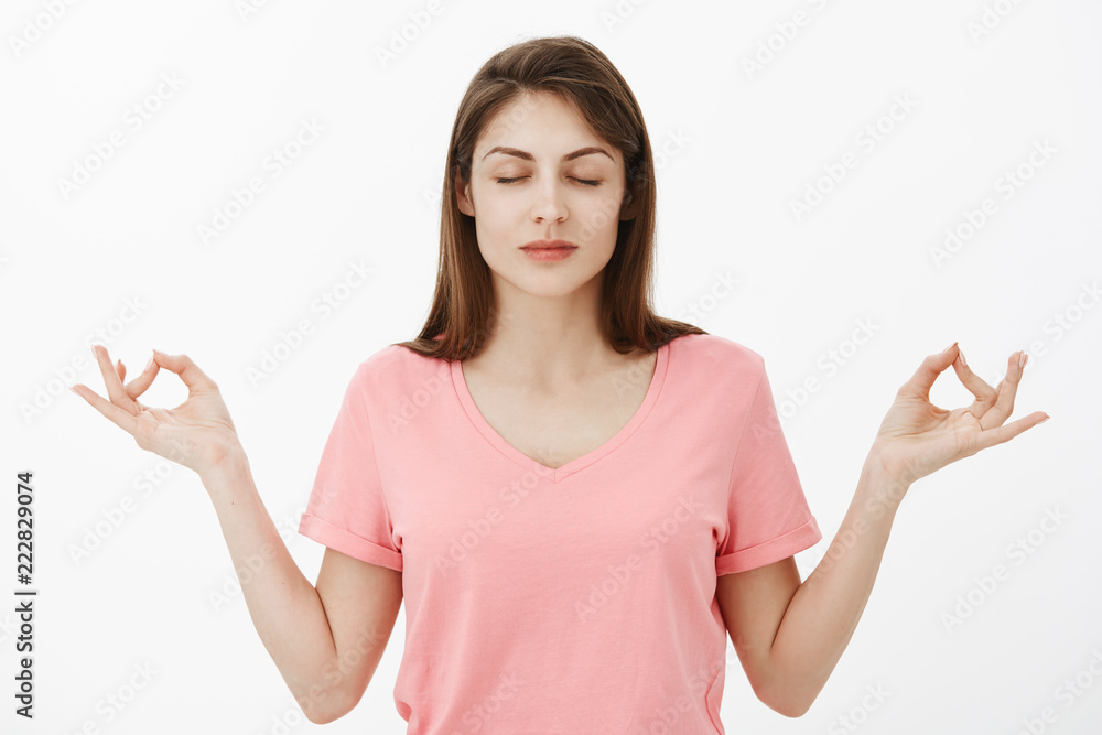 Girl inhales air and relaxes. Calm and relieved attractive young woman in pink t-shirt, standing with closed eyes and spread hands with zen gesture during meditation practice or yoga lesson Girl inhales air and relaxes. Calm and relieved attractive young woman in pink t-shirt, standing with closed eyes and spread hands with zen gesture during meditation practice or yoga lesson