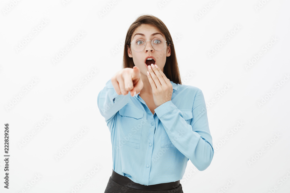 Look there, it is unbelievable. Shocked excited funny woman in glasses and blue blouse, covering opened mouth with hand while dropping jaw and pointing at camera, being amazed and impressed Look there, it is unbelievable. Shocked excited funny woman in glasses and blue blouse, covering opened mouth with hand while dropping jaw and pointing at camera, being amazed and impressed