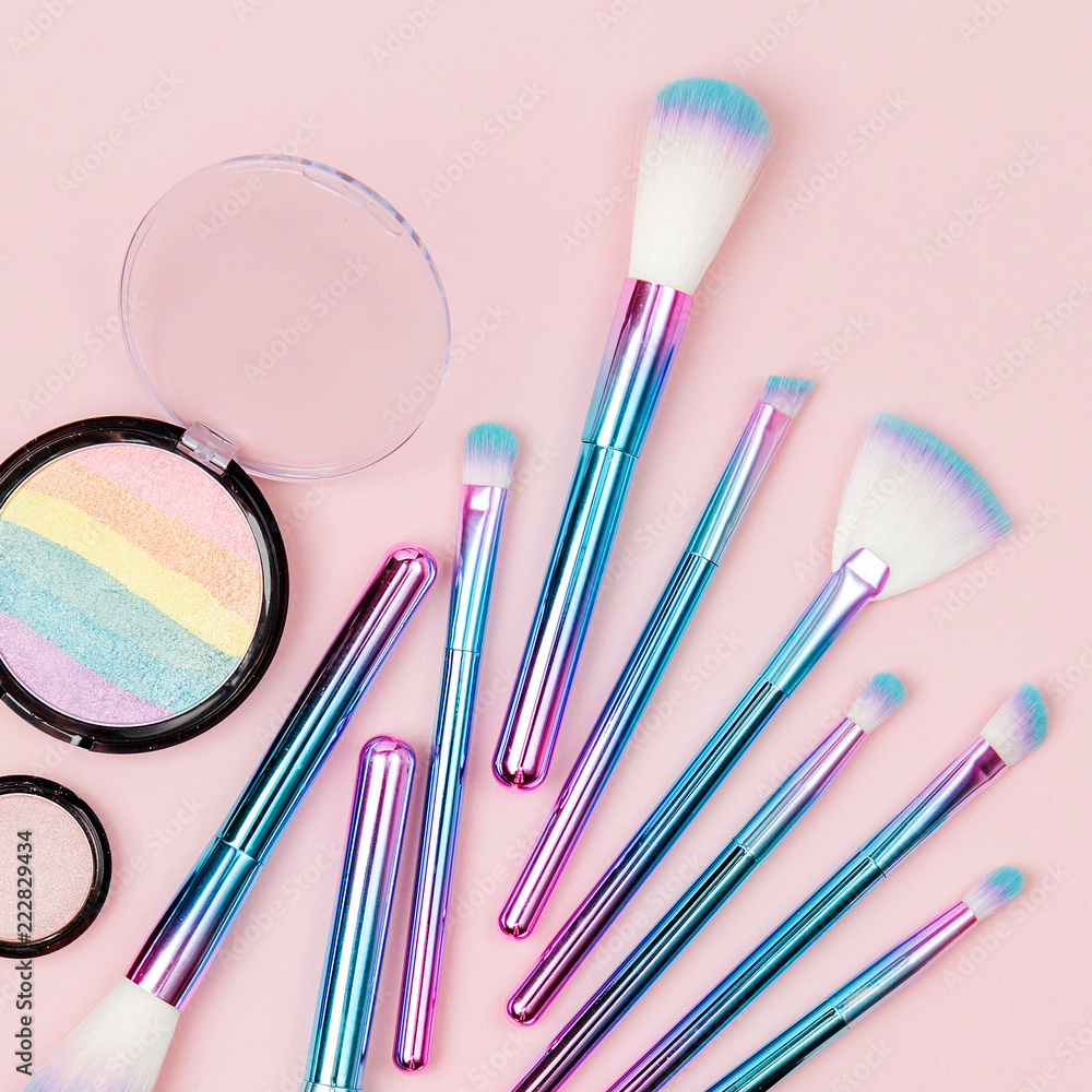 Fashion holographic colored makeup brushes with eye shadow and powder on a pastel pink background. Flat lay, top view Fashion holographic colored makeup brushes with eye shadow and powder on a pastel pink background. Flat lay, top view