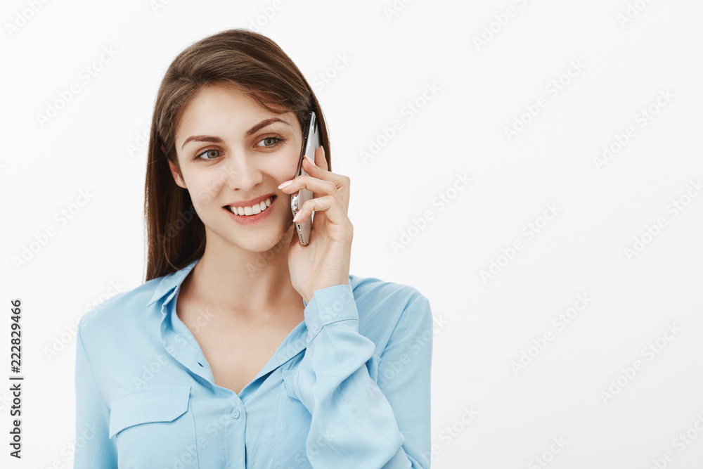 Girl calling mother from work. Portrait of positive happy cute female coworker in blue blouse, holding smartphone new ear, gazing aside and smiling, talking with friend and enjoying nice conversation Girl calling mother from work. Portrait of positive happy cute female coworker in blue blouse, holding smartphone new ear, gazing aside and smiling, talking with friend and enjoying nice conversation
