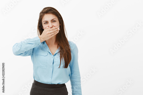 Woman needs keep mouth shut. Portrait of casual european female brunette in blue blouse, covering mouth with palm and staring at camera, keeping secret or being offended, not talking to boyfriend