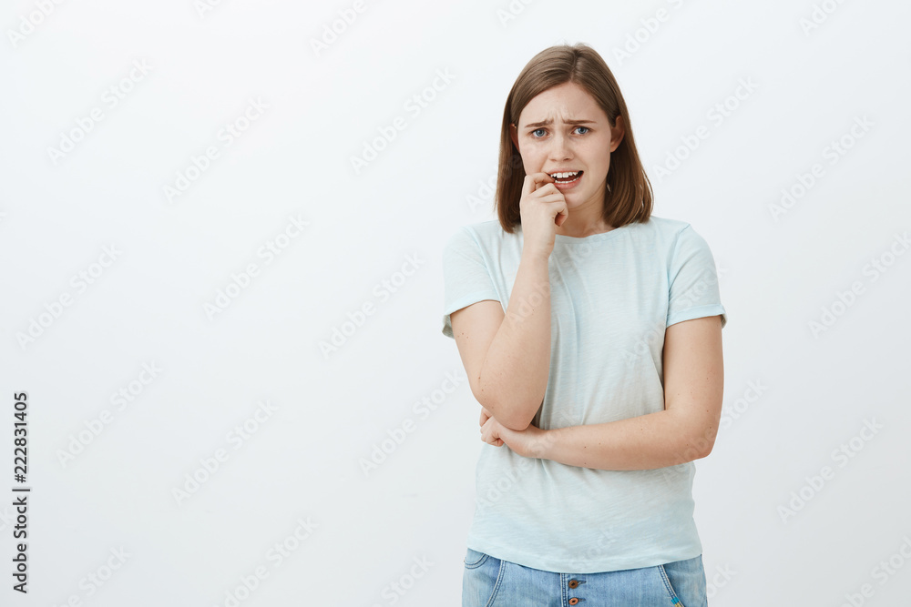 Girl going panic unsure what do. Portrait of anxious timid girlfriend in casual outfit frowning whining and biting fingernail from nervous feelings standing insecure and worried over grey background Girl going panic unsure what do. Portrait of anxious timid girlfriend in casual outfit frowning whining and biting fingernail from nervous feelings standing insecure and worried over grey background