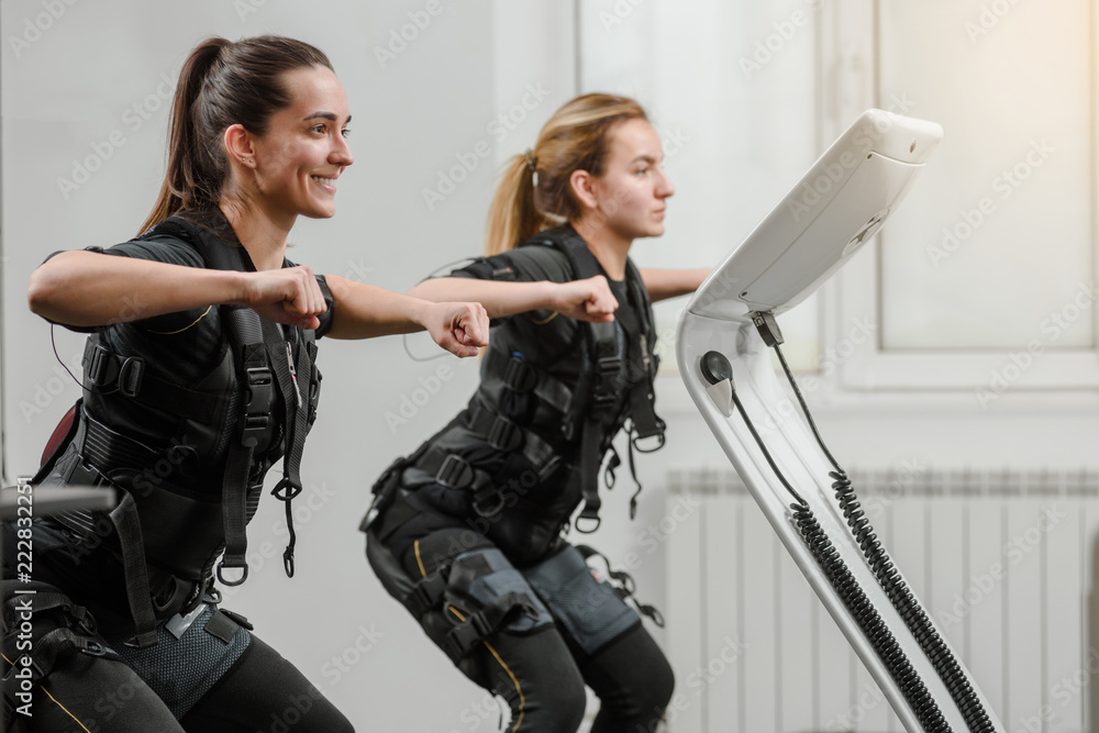 Young athletic women in EMS suits exercising in modern gym - obrazy, fototapety, plakaty 