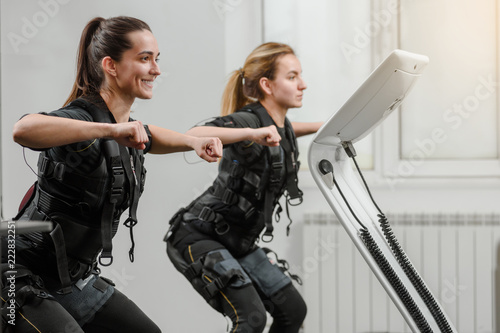 Young athletic women in EMS suits exercising in modern gym photo