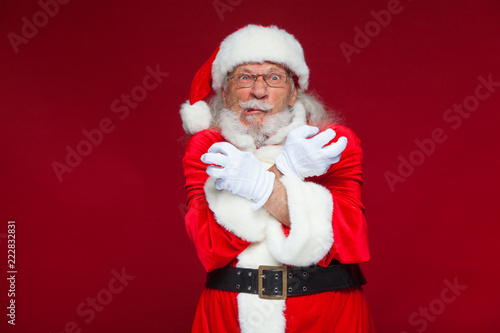 Christmas. Good Santa Claus in white gloves shows faces, grimaces, shows his tongue. Not standard behavior. Isolated on red background.