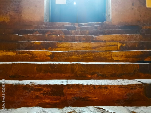 Concept of life is going to light. The staircase is made of stone as it goes up to the lighted door. Selective focus and copy space.