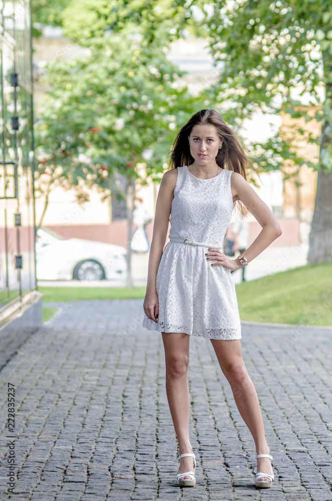 Beautiful young girl in a white summer dress near a showcase with reflection
