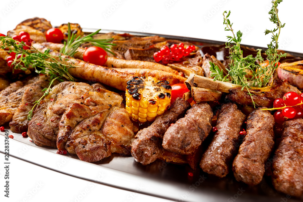 Closeup metal dish with grilled meat assortment and vegetables isolated at white background.