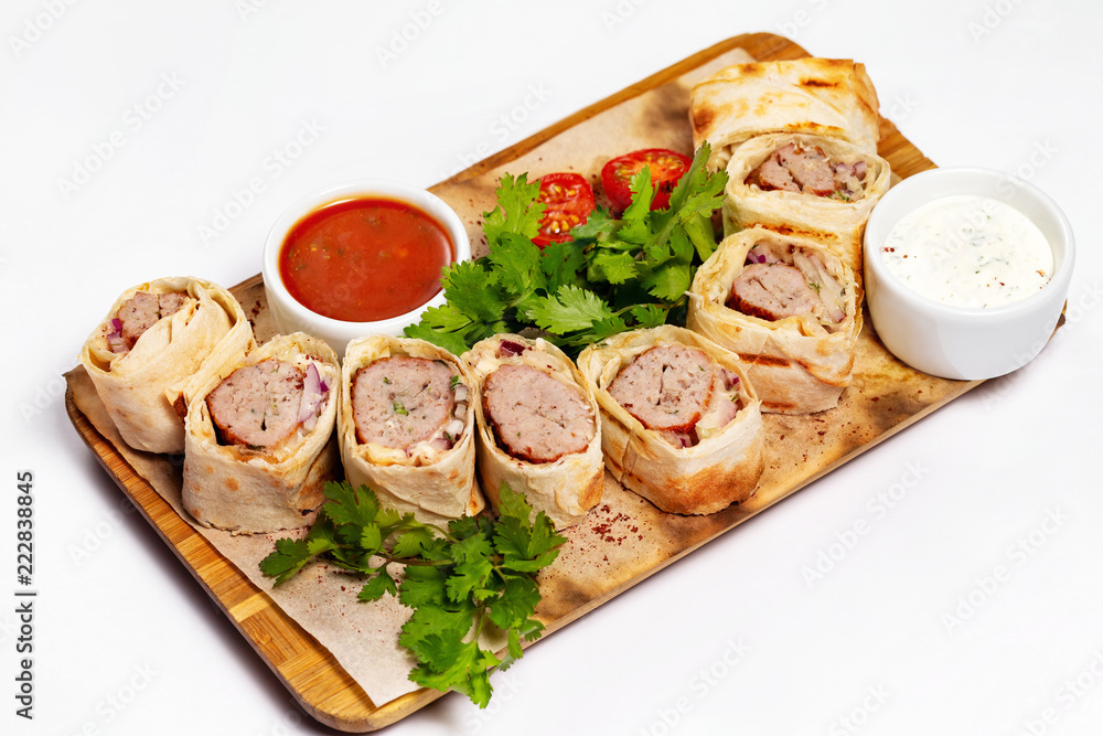 Traditional meal lula kebab - minced mutton chop slices in lavash served with sauce at wooden board isolated at white background.