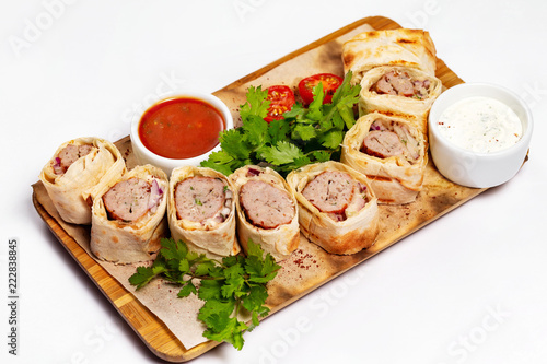Traditional meal lula kebab - minced mutton chop slices in lavash served with sauce at wooden board isolated at white background.
