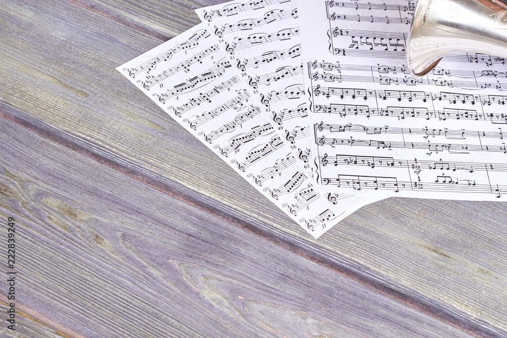 Fototapeta premium Sheets of musical notes on wooden background. Vintage trumpet on wooden background with copy space. Concept of musical education.
