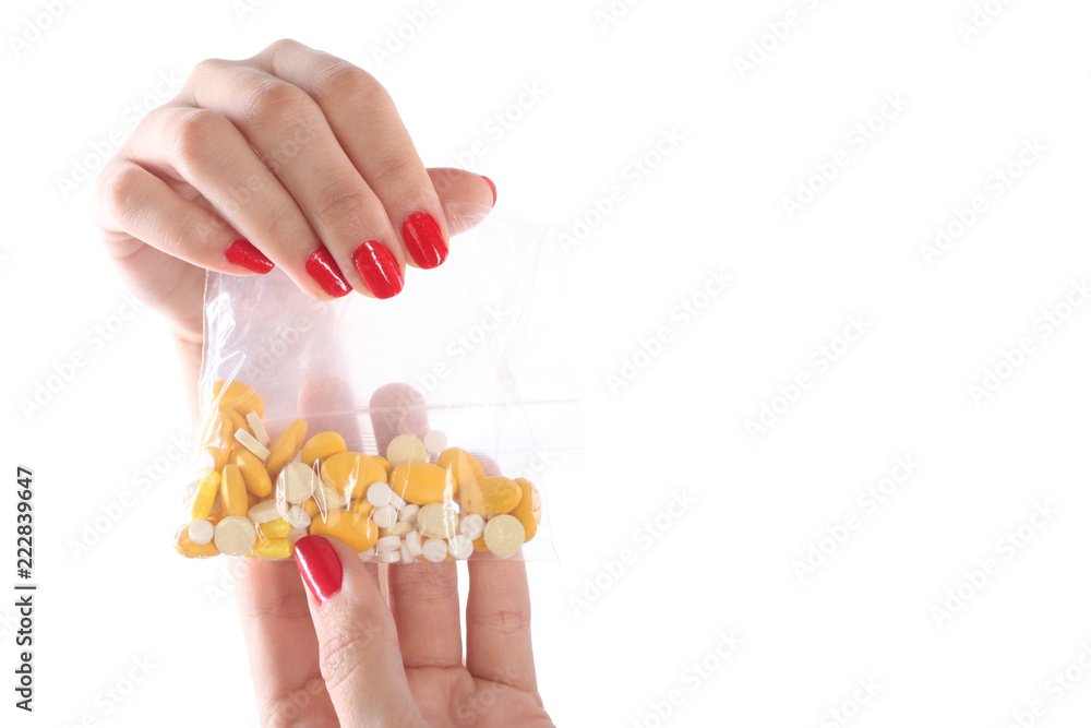 Obraz premium Female hand holding a plastic transparent bag with yellow and white pills.