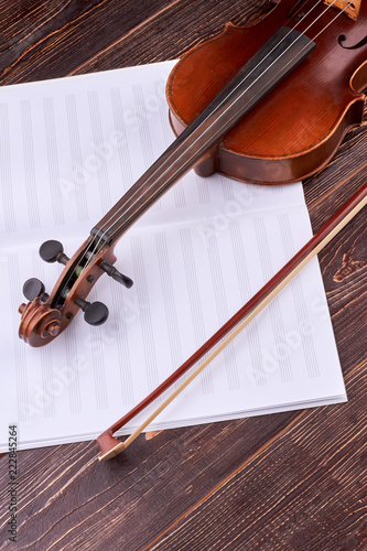 Violin and music notes book, vertical image. Violin, bow and musical notes on brown wood, top view. Lesson of classical music. photo