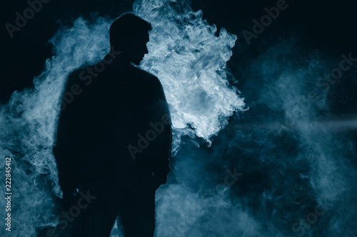 Fototapeta The man silhouette standing in the smoke. evening night time