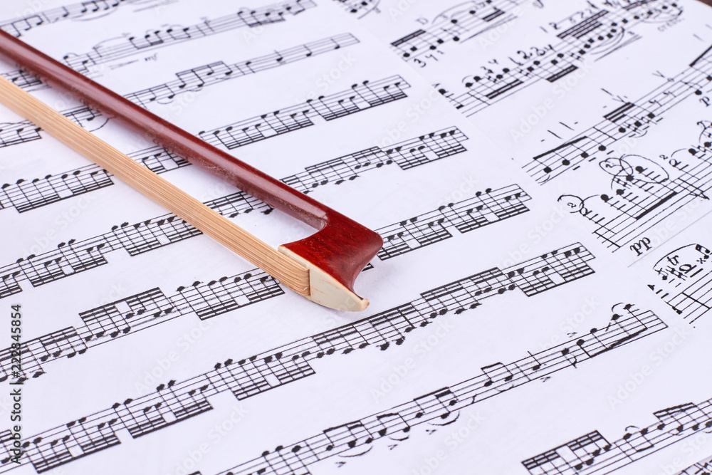 Brown violin bow on musical notes sheets. Fiddle stick on musical notes close up. Classical music background. Brown violin bow on musical notes sheets. Fiddle stick on musical notes close up. Classical music background.