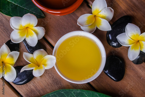 massage oil with plumeria flowers  black round stones and orange candle on wooden surface