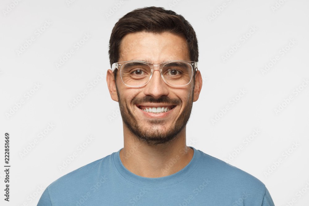 Close up shot of smiling attractive man in blue t-shirt and trendy trasparent eyeglasses isolated on gray background Close up shot of smiling attractive man in blue t-shirt and trendy trasparent eyeglasses isolated on gray background