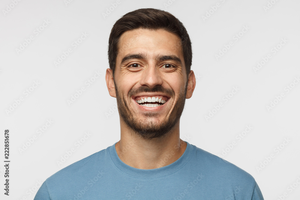 Close up horizontal shot of handsome smiling broadly unshaven young man in blue tshirt laughing out loud Close up horizontal shot of handsome smiling broadly unshaven young man in blue tshirt laughing out loud