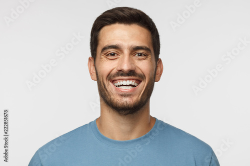 Close up horizontal shot of handsome smiling broadly unshaven young man in blue tshirt laughing out loud