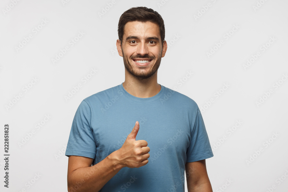 Young man isolated on grey background showing thumb up with positive emotions and happiness. Satisfaction with quality and recommendation Young man isolated on grey background showing thumb up with positive emotions and happiness. Satisfaction with quality and recommendation