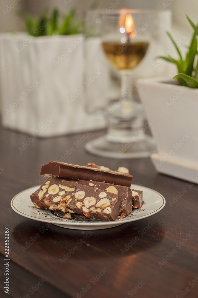 Handmade raw chocolate with hazelnuts is a healthy snack and a delicious dessert. Slice of chocolate is on a decorative plate and an olive oil candle burning on a blurred background