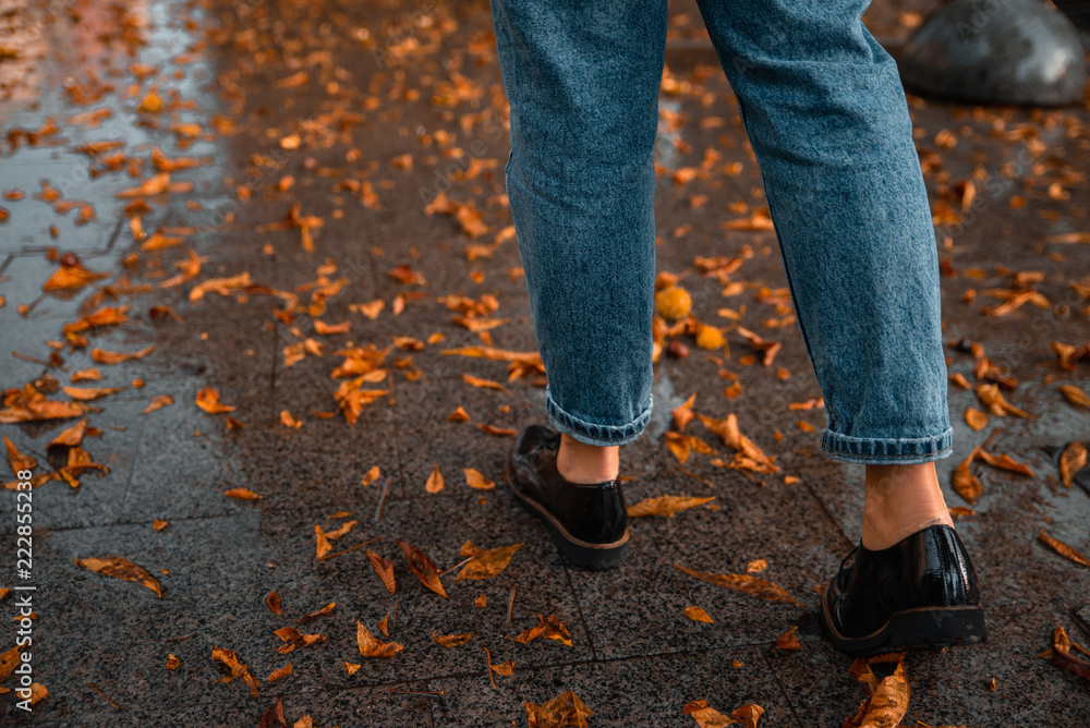 woman walking by wet streets after rain. yellow leaves on ground.