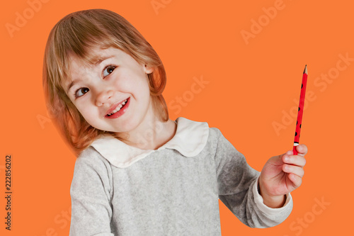 Fotografija Portrait of little baby girl holding pencil isolated on an orange background