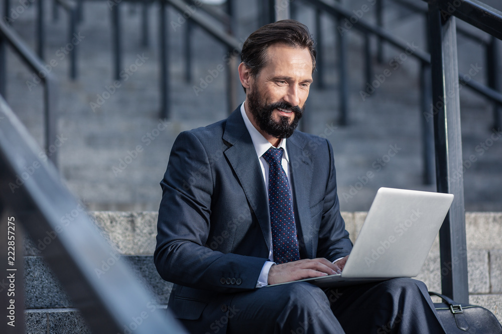 Positive bearded businessman using laptop on the staircases Positive bearded businessman using laptop on the staircases