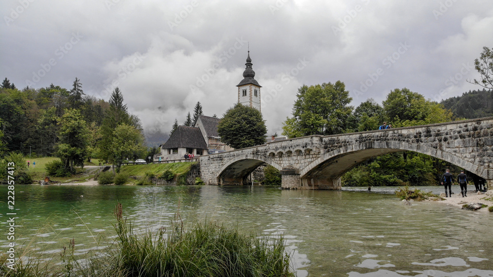 Church and bridge on Bohinj lake in slovenia. Very cloudy day