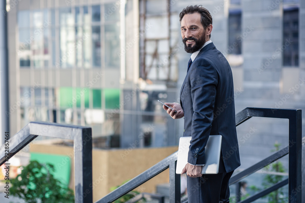 Positive professional businessman standing near a handrail
