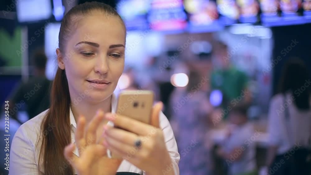 a young woman is sitting in a fast food cafe, taking selfies and looking at her photos on the smartphone screen. a young woman is sitting in a fast food cafe, taking selfies and looking at her photos on the smartphone screen.