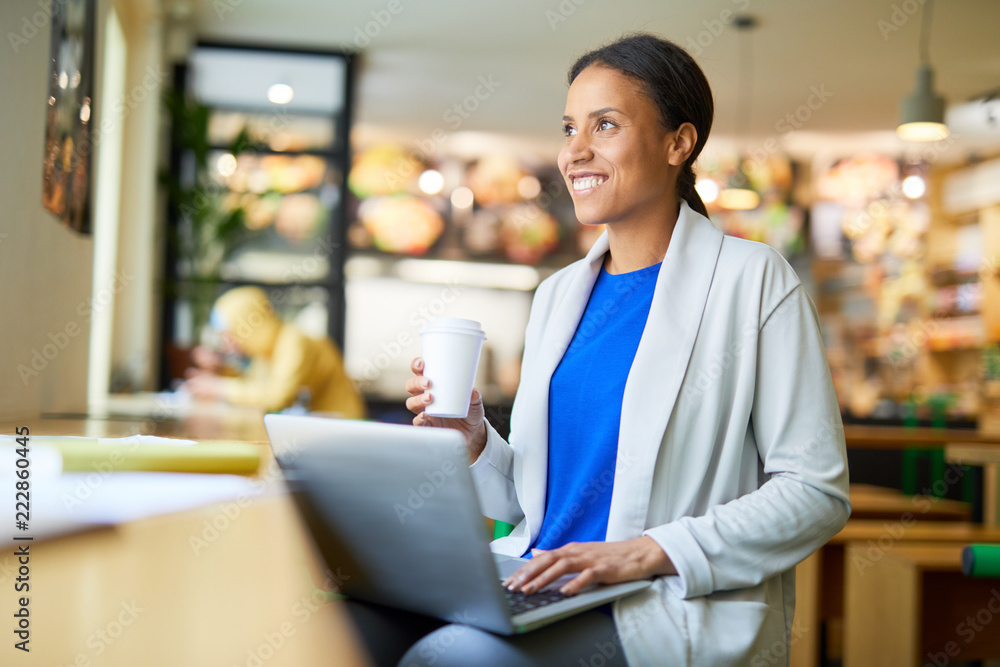 Young designer or manager with drink and laptop getting inspired in cafe while looking through window Young designer or manager with drink and laptop getting inspired in cafe while looking through window