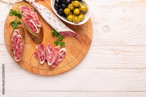 Salami and bread on white wooden background. Top view.