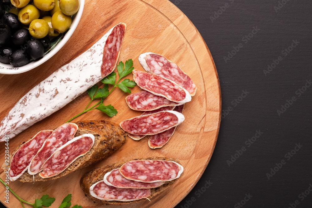 Salami and bread on black background. Top view. Copy space