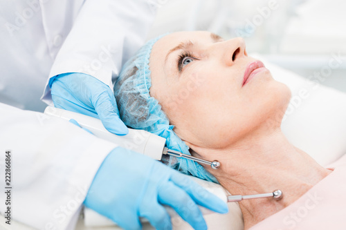Gloved cosmetician holding two steel electric rods with small spheres on ends close to client neck