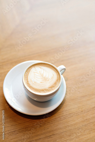 Cappuccino cup on a white saucer on a wooden table of restaurant