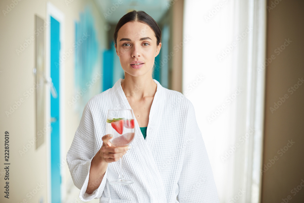 Young woman in white bathrobe holding glass of fresh fruit cocktail in spa center Young woman in white bathrobe holding glass of fresh fruit cocktail in spa center