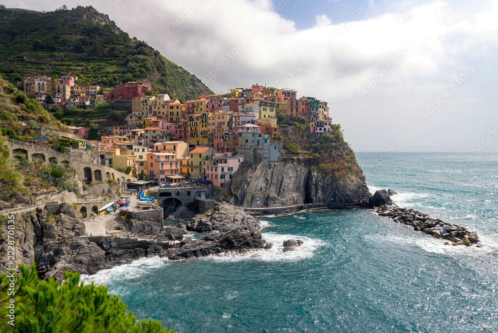 View of beautiful colorful traditional fisherman houses on a cliff over Ligurian sea on cloudy day in Manarola village, Cinque Terre national park, Liguria, La spezia province, Italy.
