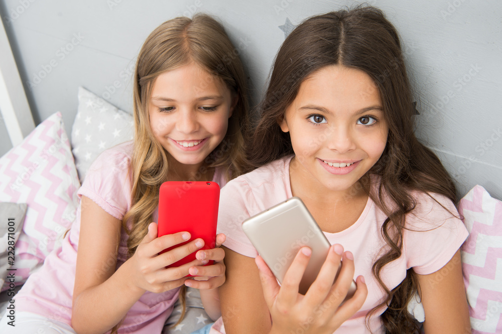 Pajamas party concept. Girlish leisure happy childhood. Girls long hair with smartphones use modern technology. Lets take selfie. Send photo your friends social network. Kids taking selfie in bedroom Pajamas party concept. Girlish leisure happy childhood. Girls long hair with smartphones use modern technology. Lets take selfie. Send photo your friends social network. Kids taking selfie in bedroom