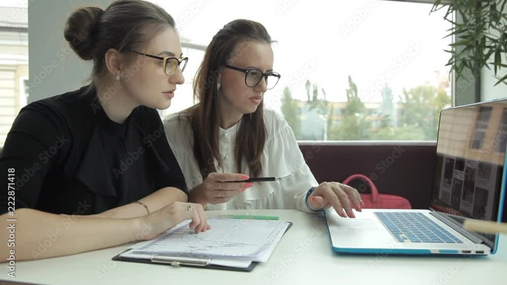 Two girls are sitting in a cafe, using a laptop and discussing business ideas Two girls are sitting in a cafe, using a laptop and discussing business ideas