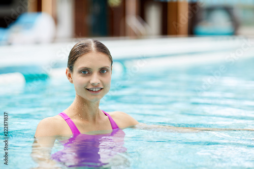 Young blonde woman looking at you while enjoying spa swimming at summer resort